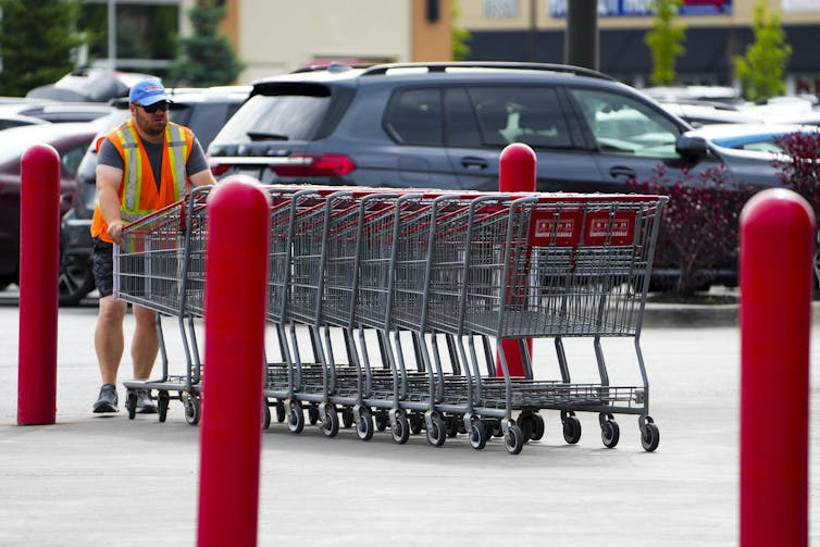 A worker pushing a row of shopping carts towards the entrance of a store