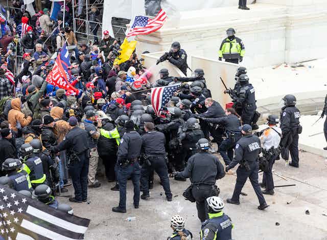 A crowd of protestors waving Trump flags are storming the U.S. Capitol while police officers try to hold them back.