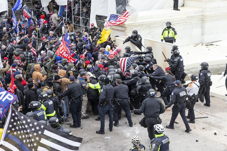 A crowd of protestors waving Trump flags are storming the U.S. Capitol while police officers try to hold them back.