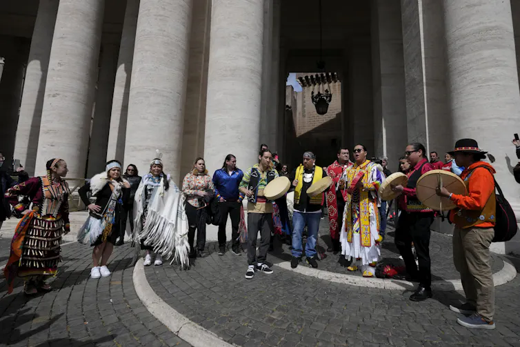 Drummers are seen standing in front of pillars.
