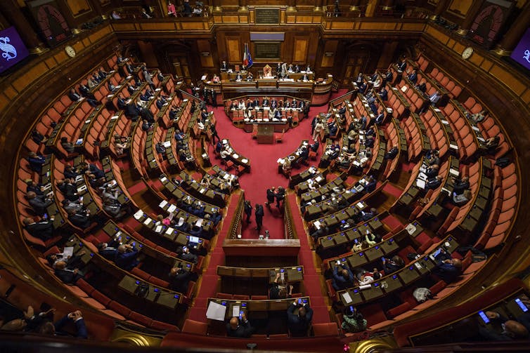 An aerial shot shows the Italian parliament with circular seating.