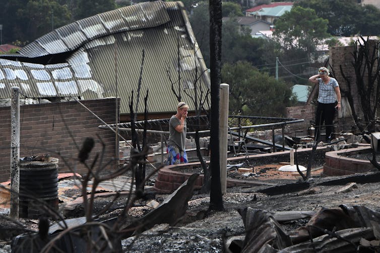 Two women stand in the remains of a burnt-out home