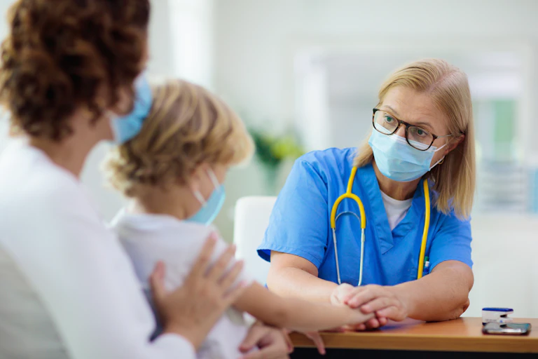 Una médico atiende a un menor sentado sobre su madre.