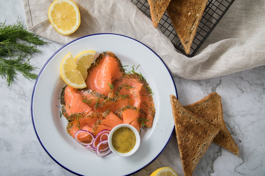 A place of salmon covered in dill and served with lemons, alongside wholegrain bread.