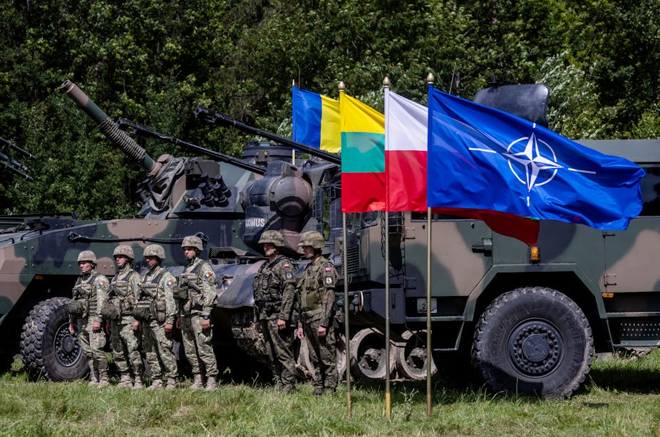 Des soldats roumains et polonais montent la garde, les drapeaux de l'OTAN, de la Pologne, de la Lituanie et de l'Ukraine sont visibles 