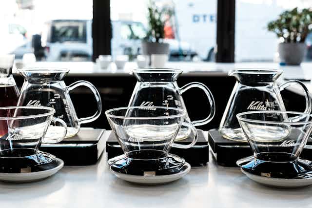 a row of glass espresso mugs in front of a row of beakers