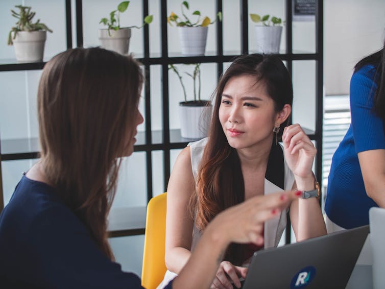 A woman is chatting with a workmate. Her face looks perplexed.