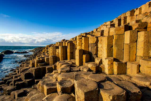 Photo of Giant's Causeway basalt columns with ocean and blue sky in background.