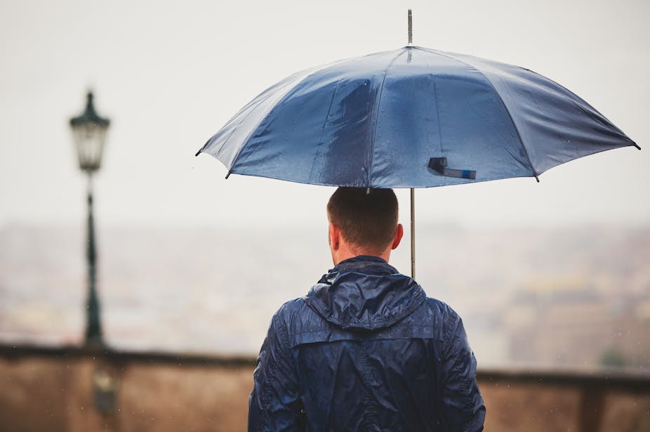 A man stands under an umbrella.
