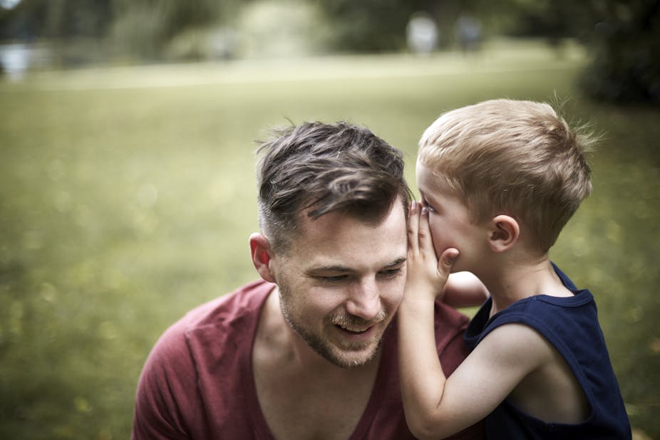 A boy whispering into his father's ear.