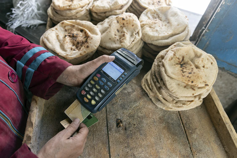 Trader standing next to a tray with piles of flat bread. She's has a speed point machine and bank cards in her hands.