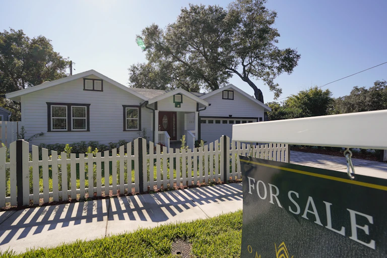 A for sale sign sits in front of a white house with a white picket fence