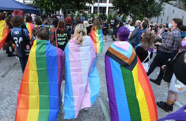 Students draped in rainbow and non-binary flags attend a protest.