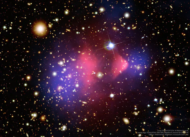 Cluster of galaxies displayed in hues of pink and purple against a black cosmic background.
