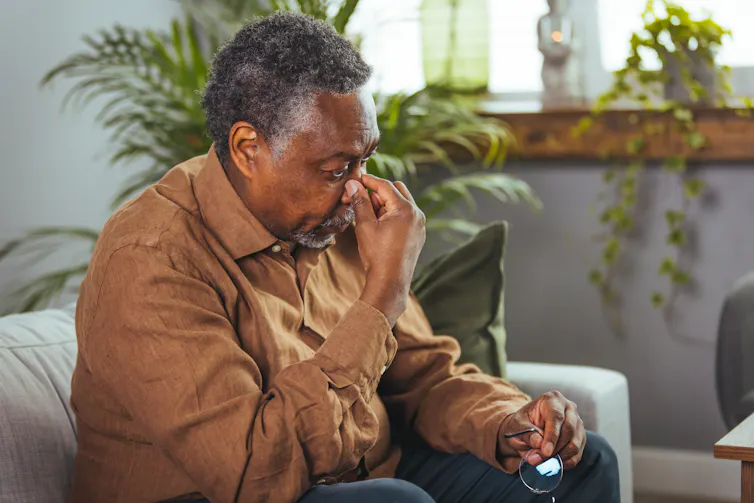 A senior man sitting on a couch appears to have a headache.