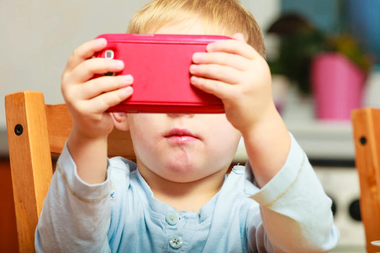 Un niño maneja un teléfono móvil rojo que le tapa ojos y nariz.
