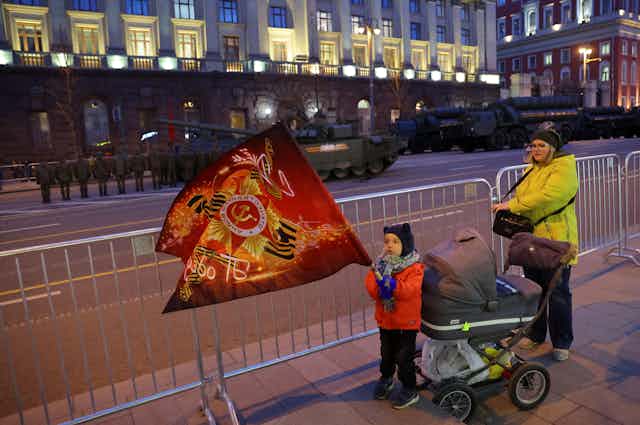 A child holds a flag as Russian service members drive tanks and other military vehicles along a street during a rehearsal for the Victory Day military parade in Moscow, Russia May 4, 2022.