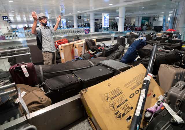 A man holds up both hands as he stands among dozens of bags at an airport baggage conveyer