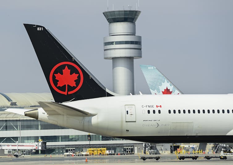 An Air Canada jet is in the foreground while the air traffic control tower of Pearson Airport is in the background.