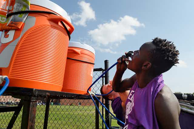 Two young male athletes drink with hoses from large Gatorade coolers.