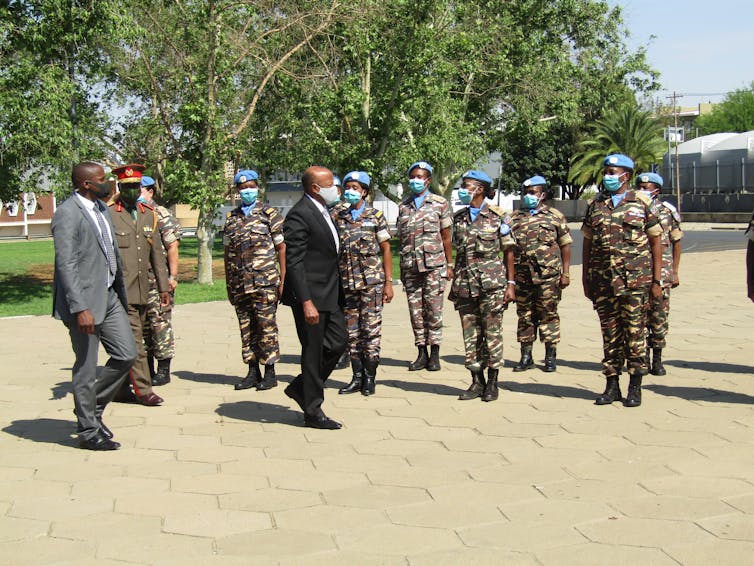 Two men in suits walk past a row of female peacekeepers in camo with blue hats