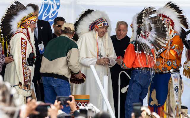 Pope Francis seen in a headdress wit Indgenous delegates in full regalia.