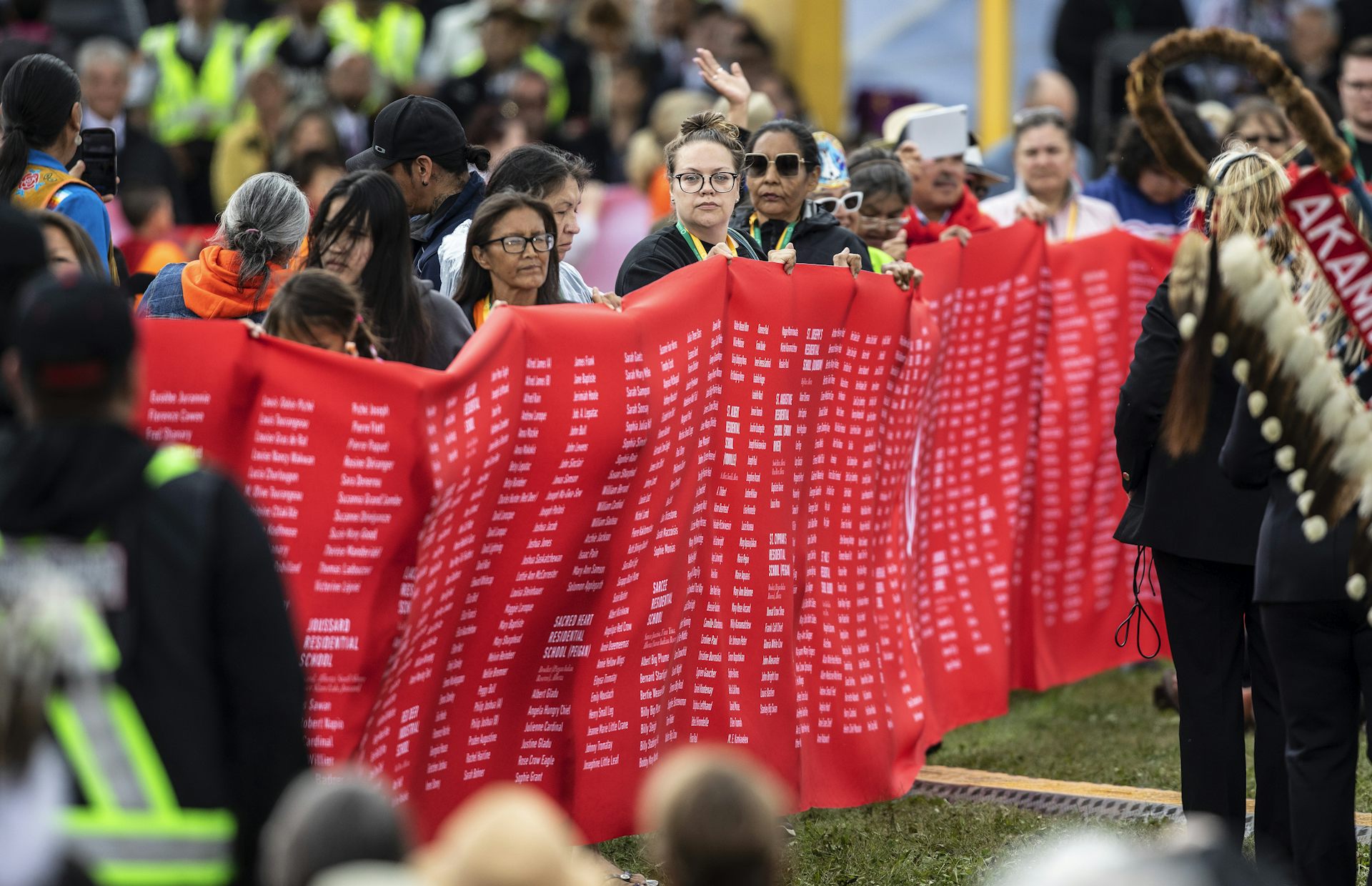 People holding a red banner with filled with many names in small font.
