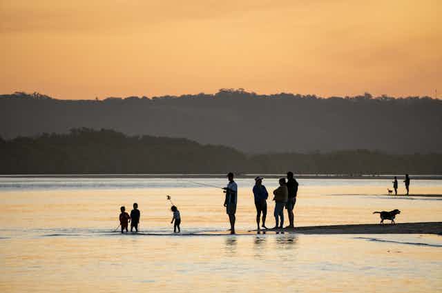 Adults and children fishing and playing at the beach at sunset