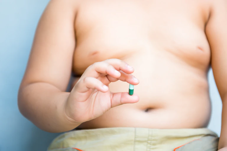 Una persona obesa con el torso a la vista muestra una píldora verde en la mano.