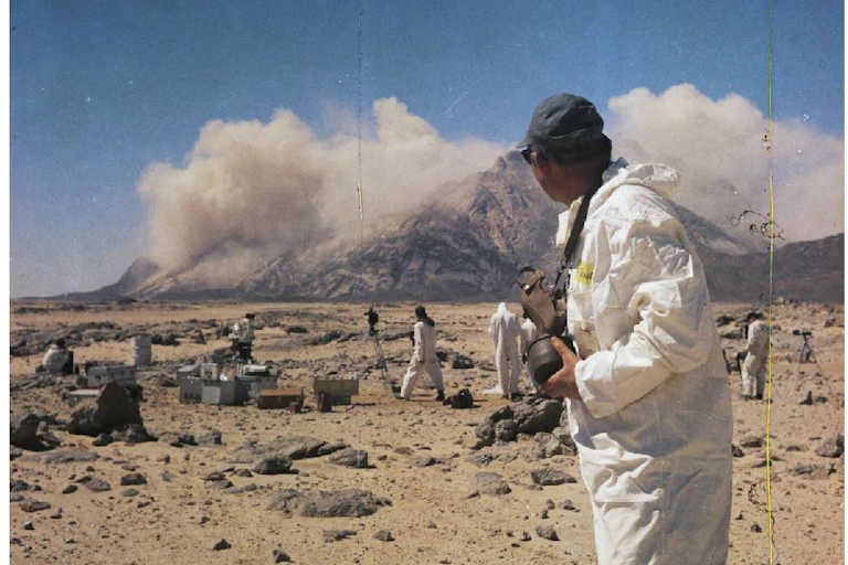 explosion behind a moutain, there is a man looking at it in the foreground