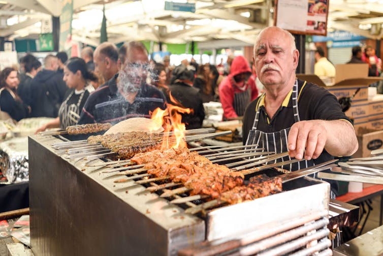 Man turns kebab skewers in market