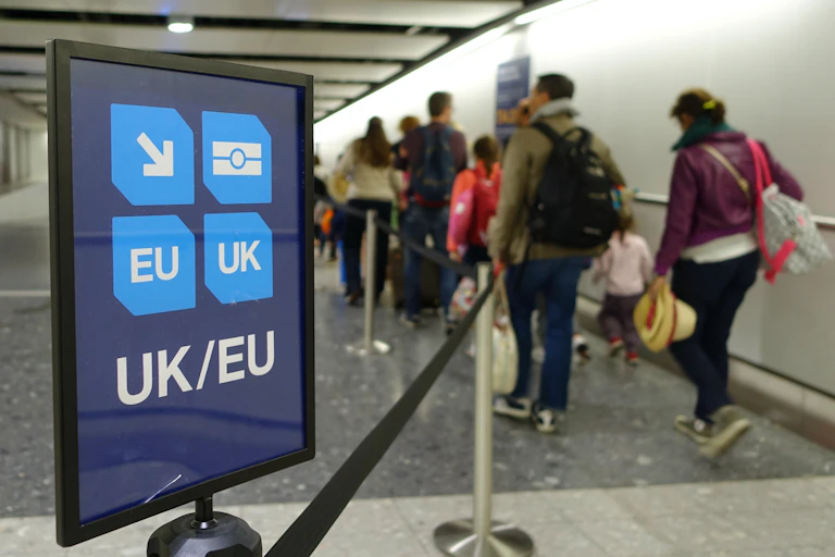 A UK/EU passport lane sign at an airport, with families walking by