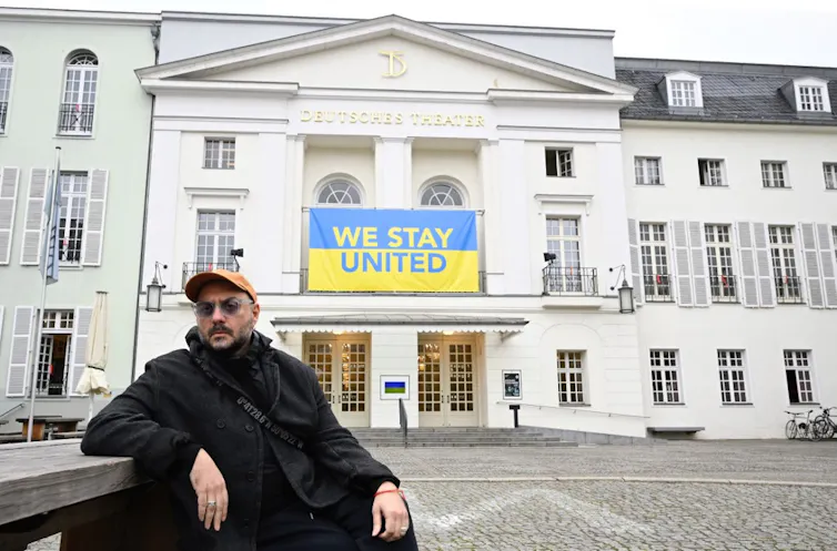 Kirill Serebrennikov devant le Deutsches Theater à Berlin, où est affichée une banderole aux couleurs du drapeau ukrainien proclamant « We Stand United »