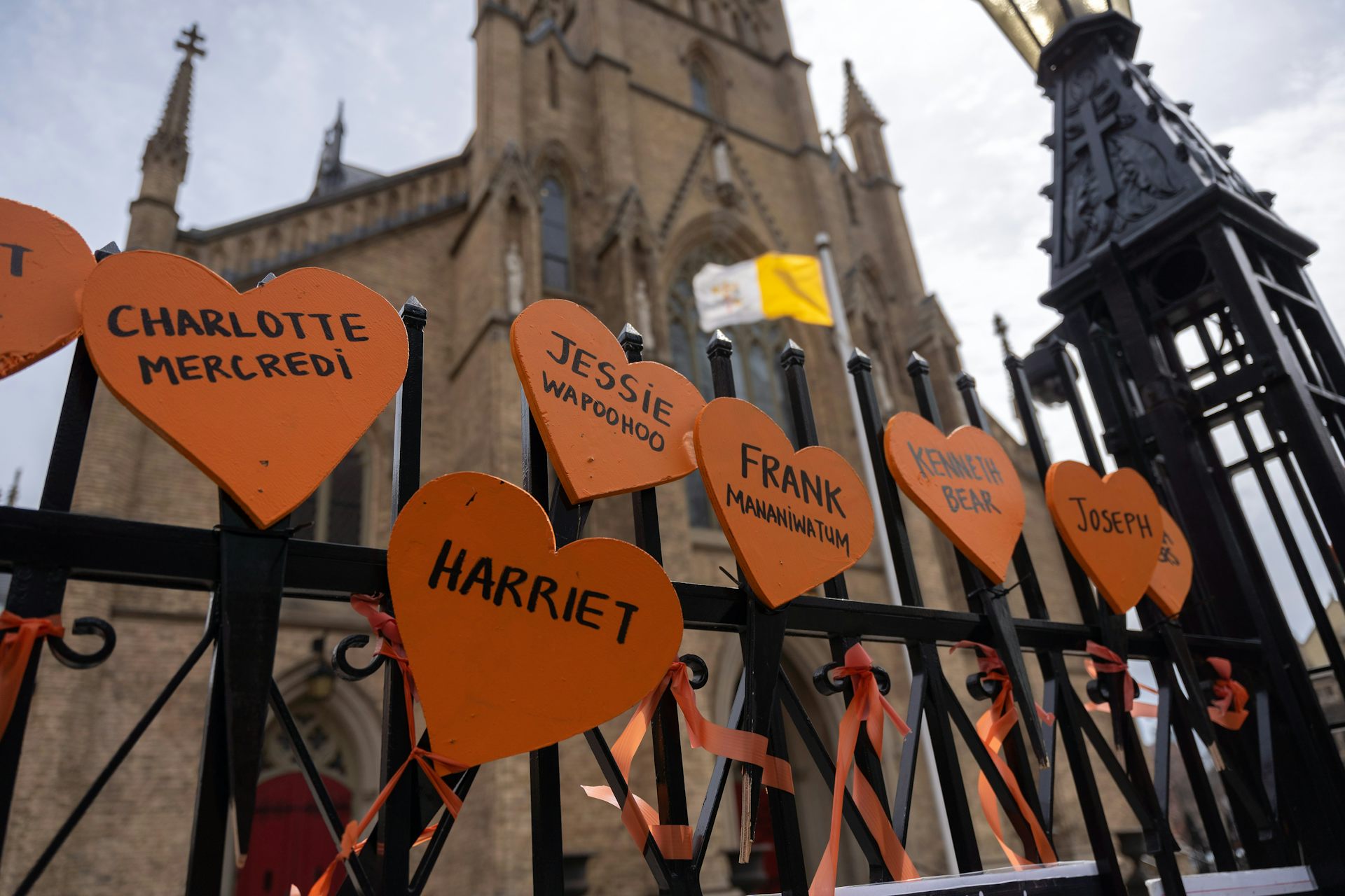 Signs printed with the names of Residential School victims are tied to the iron gates surrounding a cathedral.