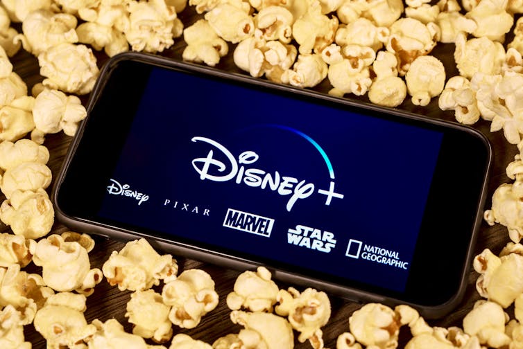 Smartphone with Disney Plus logo, surrounded by popcorn