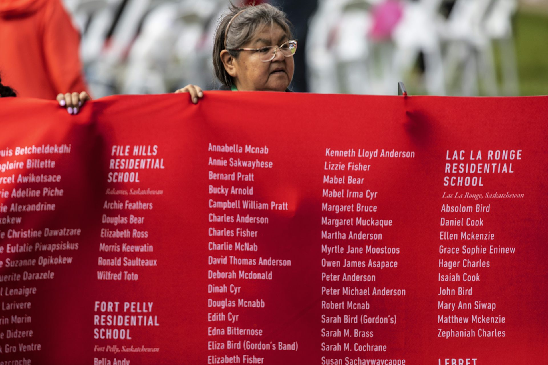 A woman holds a red banner with hundreds of names on it.