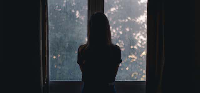 A woman shrouded in darkeness look out of an open window.