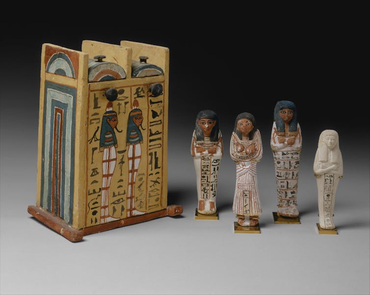 Caja de pequeñas estatuas egipcias con varias de esas estatuas junto a ella.