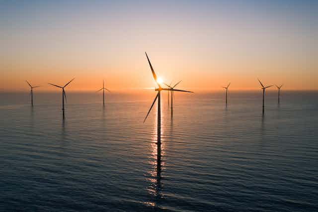 An offshore wind farm (wind turbines over water), with a sunset in the background