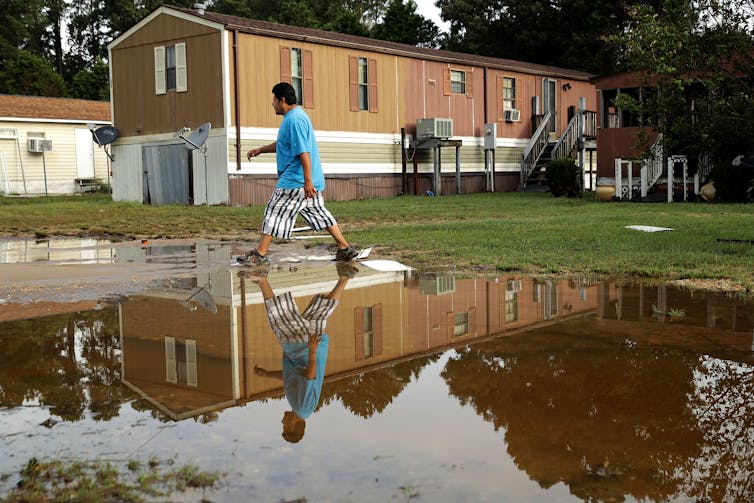 A man walks past large puddles and manufactured homes.