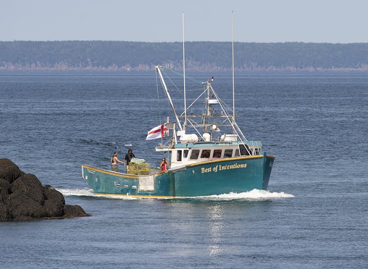 A green-hulled fishing boat moving through blue water around a rocky point of land.