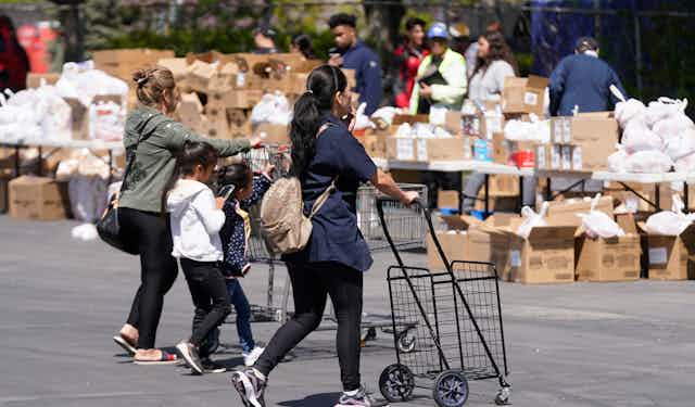 Two young women and a child push carts toward tables full of food