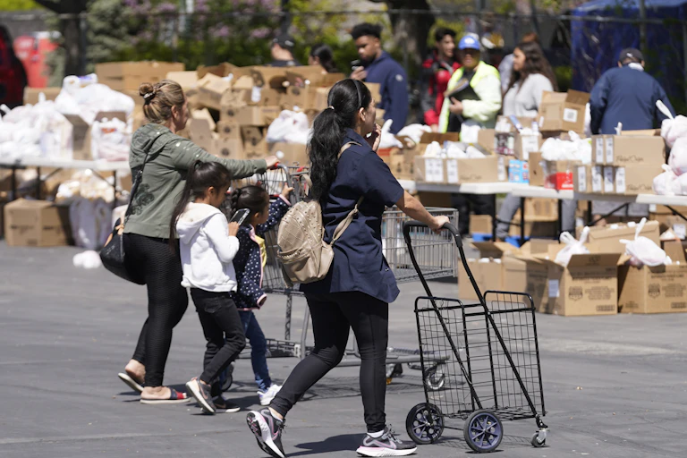 Two young women and a child push carts toward tables full of food