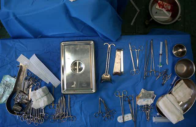 Two tables draped in blue cloth with surgical implements on them