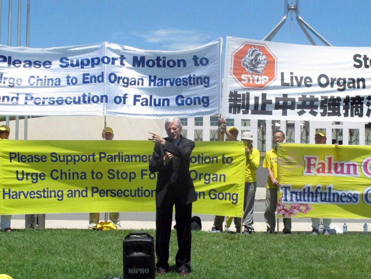 A man standing outdoors in front of signs opposing forced organ harvesting in China