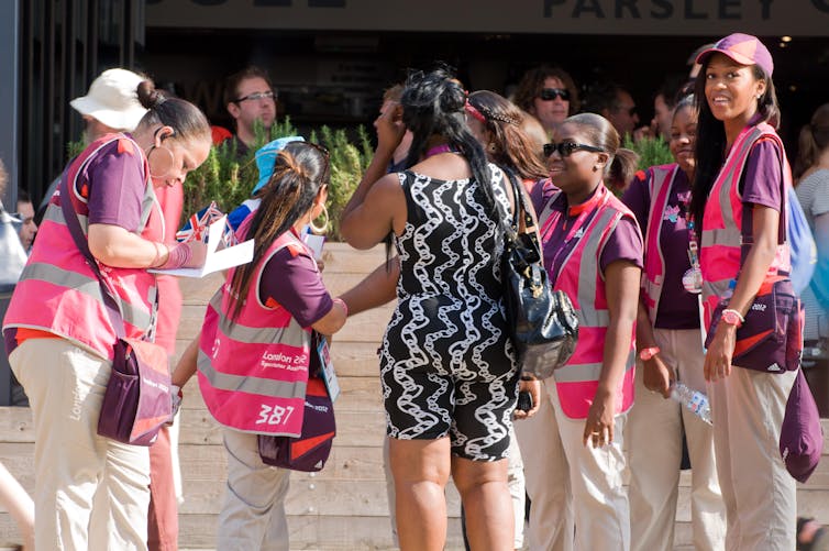 Volunteers in pink vests help visitors outside.