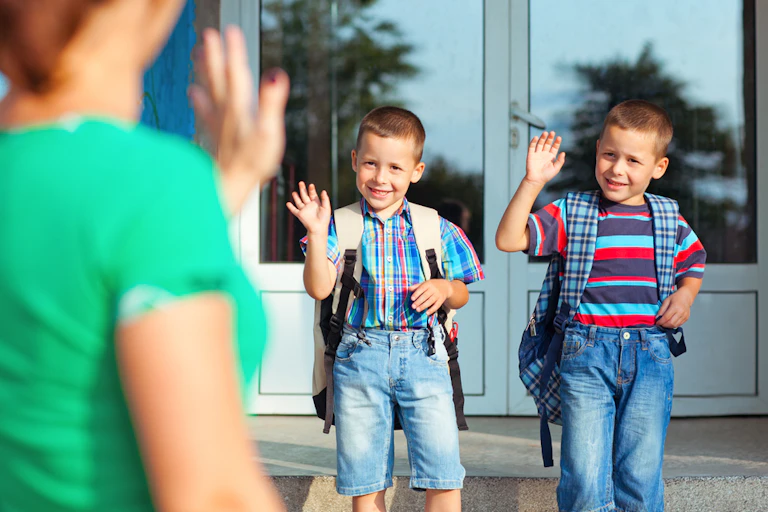 Deux enfants disent au revoir à leur mère avant d'entrer dans l'école