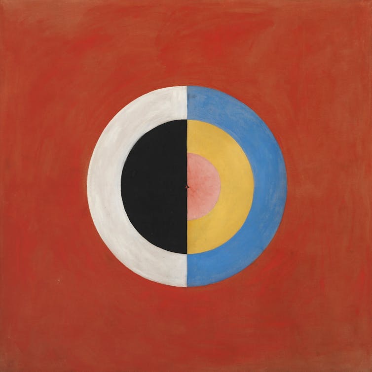 An abstract painting, red background with a circle superimposed on it. Half a circle has a blue border, the other half a white border, and inside the filling is half black, half yellow.