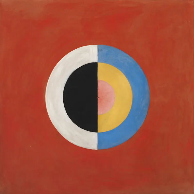 An abstract painting, red background with a circle superimposed on it. Half a circle has a blue border, the other half a white border, and inside the filling is half black, half yellow.