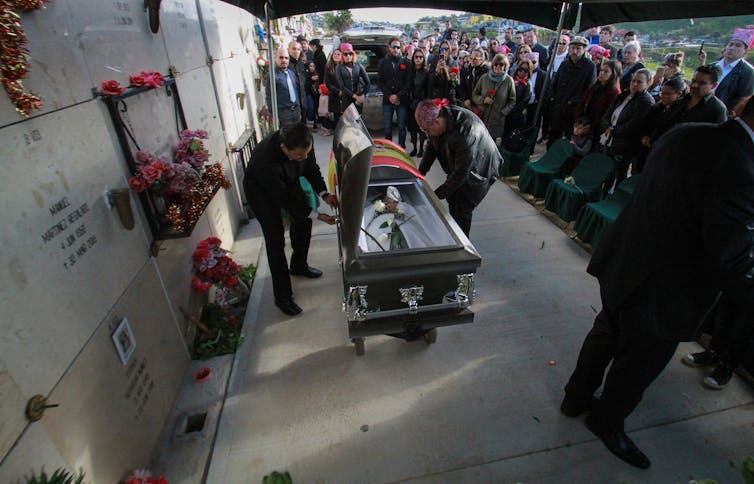 A coffin bearing the funeral of a man shot dead in Tijuana, Mexico, is wheeled into a funeral service as a crowd watches.
